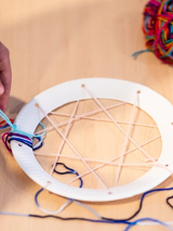 grafika przedstawia łapacza snów w trakcie wykonywania: papierowy okrąg i przeplatane na nim kolorowe nici