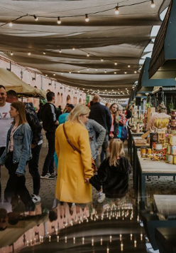Ludzie chodzący pod zadaszonymi straganami.