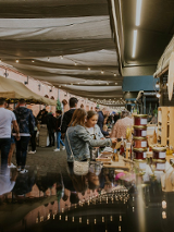 Ulica pod baldachimami pełna stoisk, a wśród nich chodzą ludzie i oglądają lub kupują wyroby rzemieślnicze.