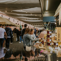 Ulica pod baldachimami pełna stoisk, a wśród nich chodzą ludzie i oglądają lub kupują wyroby rzemieślnicze.