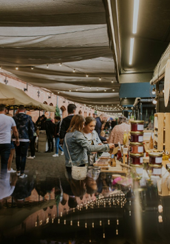 Ulica pod baldachimami pełna stoisk, a wśród nich chodzą ludzie i oglądają lub kupują wyroby rzemieślnicze.