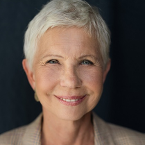 Zdjęcie uśmiechniętej kobiety w średnim wieku, ubranej w białą buzkę i beżową marynerkę w kratę.