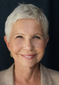 Zdjęcie uśmiechniętej kobiety w średnim wieku, ubranej w białą buzkę i beżową marynerkę w kratę.