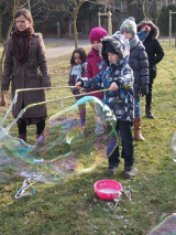 Zdjęcie przedstawia bawiące się dzieci na dworze z bańkami mydlanymi na półkolonii.