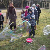 Zdjęcie przedstawia bawiące się dzieci na dworze z bańkami mydlanymi na półkolonii.