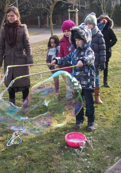 Zdjęcie przedstawia bawiące się dzieci na dworze z bańkami mydlanymi na półkolonii.
