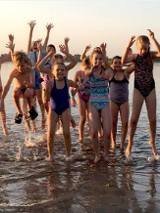 Na zdj eciu znajduje się grupa dzieci, która skaczę w jeziorze z podniesionymi ku górze rękoma.