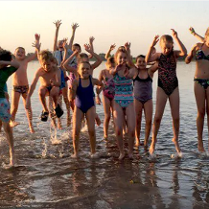 Na zdj eciu znajduje się grupa dzieci, która skaczę w jeziorze z podniesionymi ku górze rękoma.