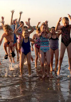 Na zdj eciu znajduje się grupa dzieci, która skaczę w jeziorze z podniesionymi ku górze rękoma.