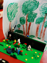 Na zdjęciu znajduje się budowla lego, sześć figurek ustawionych na zielonych podstawkach najprawdopodobniej imitują walkę.