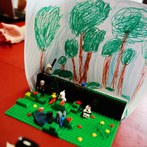 Na zdjęciu znajduje się budowla lego, sześć figurek ustawionych na zielonych podstawkach najprawdopodobniej imitują walkę.