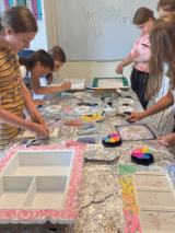 Zdjęcie przedstawia grupę dzieci, która zebrana w okół stoł wykonuje rękodzieła.