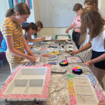 Zdjęcie przedstawia grupę dzieci, która zebrana w okół stoł wykonuje rękodzieła.