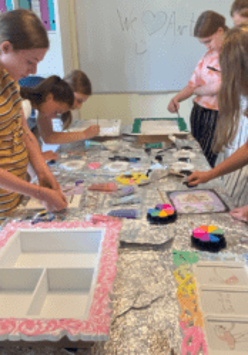 Zdjęcie przedstawia grupę dzieci, która zebrana w okół stoł wykonuje rękodzieła.