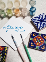 Na zdjęciu znajdują się 4 kafelki w różnych rozmiarach, na jednym widnieje napis "Azulejo", a pozostałe trzy są pomalowane. Na zdjęciu znajdują się również farbki oraz dwa pędzle.