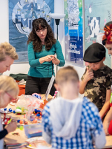 Na zdjęciu uczestnicy warsztatów pochylają się nad stołem, na którym leżą różne kolorowe przedmioty