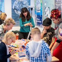 Na zdjęciu uczestnicy warsztatów pochylają się nad stołem, na którym leżą różne kolorowe przedmioty