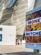 Przed wejściem reklmay o wystawie w środku muzeum. W tle nowoczesne przeszkolne wejście do muzeum.