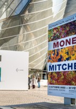 Przed wejściem reklmay o wystawie w środku muzeum. W tle nowoczesne przeszkolne wejście do muzeum.