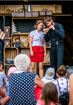 Zdjęcie przedstawie fragment ze spektaklu. Na zdjęciu znajdują się dwie osoby na scenie, oraz tłum pod nią.