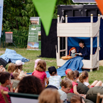 Mini scena na trawie, gdzie Pani persofinikuje postać lalki. Przed nią siedzą dzieci na trawie.