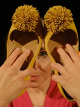 Kobieta trzyma w rękach dwa damskie buty z pomponami, zakrywa nimi część twarzy.