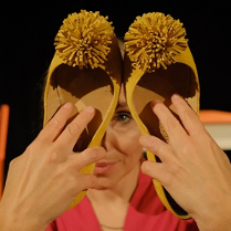 Kobieta trzyma w rękach dwa damskie buty z pomponami, zakrywa nimi część twarzy.