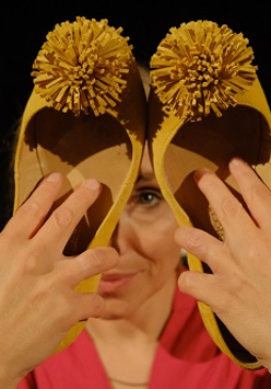 Kobieta trzyma w rękach dwa damskie buty z pomponami, zakrywa nimi część twarzy.