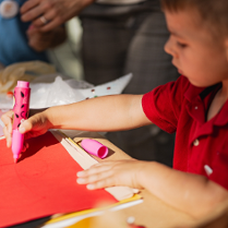 Zdjęice chłopca rysującego flamastrem na czerwonej kartce papieru.