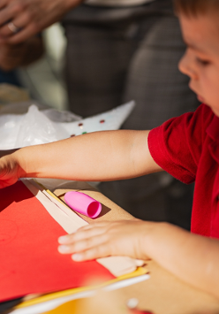 Zdjęice chłopca rysującego flamastrem na czerwonej kartce papieru.