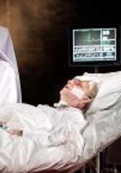 na łóżku szpitalnym leży męzczyzna podłączony do aparatury medycznej, obok stoi siostra zakonna