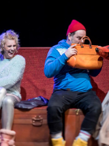 Zdjęcie ze spektaklu: trzy osoby siedzące na ławce. Mężczyzna trzyma przed sobą torebkę, zasłania się przed psem animowanym przez jedną z dwóch aktorek.