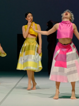 Zdjęcie dwóch tancerek w kolorowych spódnicach i topach na scenie