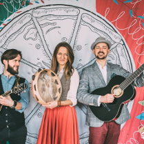 na zdjęciu dwóch mężczyzn i kobieta grający na instrumentach muzycznych na scenie, w tle za nimi duży rysunek pizzy