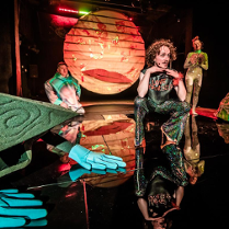 Zdjęcie trzech aktorów na scenie wśród elementów scenicznych dekoracji.