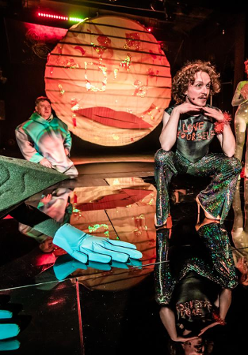 Zdjęcie trzech aktorów na scenie wśród elementów scenicznych dekoracji.