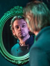 Zdjęcie mężczyzny przeglądającego się w lustrze ze zdobioną ramą.