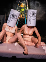 Zdjęcie dwóch siedzących kobiet w strojach bikini, z nałóżonymi na głowy tubami. Na każdej tubie narysowane jest oko, z którego lecą łzy.