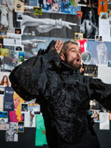 Zdjęcie mężczyzny w czarnym stroju na tle kolorowych zdjęć.