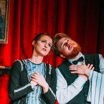 Mężczyzna i kobieta, stojący obok siebie z uniesionymi twarzami ku górze i złożonymi rękami na piersiach.