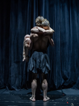 na scenie stoi tancerz, odwrócony tyłem, na rękach trzyma kobietę, która pochyla głowę do jego ramienia i obejmuje go za szyję