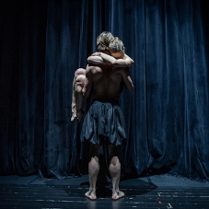 na scenie stoi tancerz, odwrócony tyłem, na rękach trzyma kobietę, która pochyla głowę do jego ramienia i obejmuje go za szyję