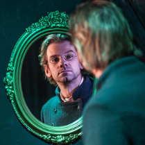 Zdjęcie mężczyzny przeglądającego się w lustrze ze zdobioną ramą.