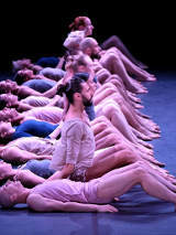 Zdjęcie tancerzy w rzędzie, z których część siedzi, a część leży na podłodze