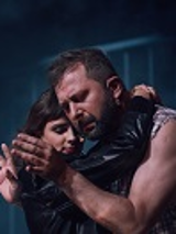 Kobieta i mężczyzna w uścisku, mężczyzna patrzy na swoje dłonie. Ciemno-niebieskie tło.