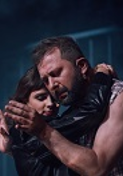 Kobieta i mężczyzna w uścisku, mężczyzna patrzy na swoje dłonie. Ciemno-niebieskie tło.