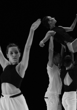 Czarno-białe zdjęcie tancerzy. Na pierwszym planie młoda kobieta z uniesionymi rękami do góry, na drugim planie trzy osoby unoszą kobietę na wyciągniętych do góry rękach.