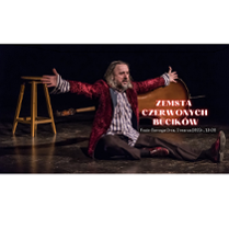 zdjęcie przedstawia aktora siedzącego na scenie, ubranego w wiśniową brokatową marynarkę, koszulę w błękitne pionowe paski oraz ciemne spodnie. Ręce ma rozłożone. Patrzy na widownię. Za aktorem po lewej stronie stoi wysoki stołek, a po prawej leży kontrabas.