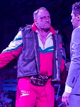 Dwóch mężczyzn stojących naprzeciwko siebie, jeden eleganco ubrany w garnitur, drugi w sportowym dresie i ortalionowej kamizelce.