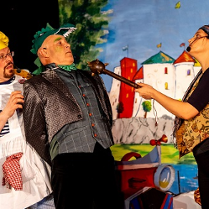 Trójka aktorów w strojach scenicznych (między innymi kucharza i smoka), w tle rysunek zamku.